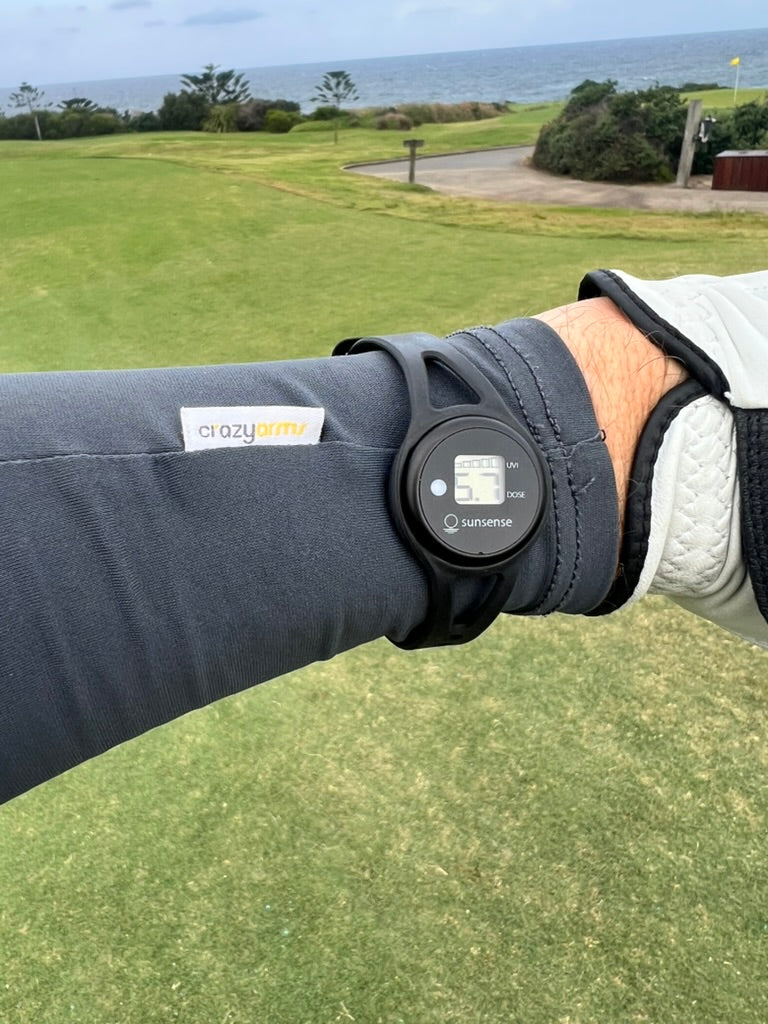 Golfer wearing a Crazy Arms sun sleeve with a UV meter on the wrist, on a coastal golf course