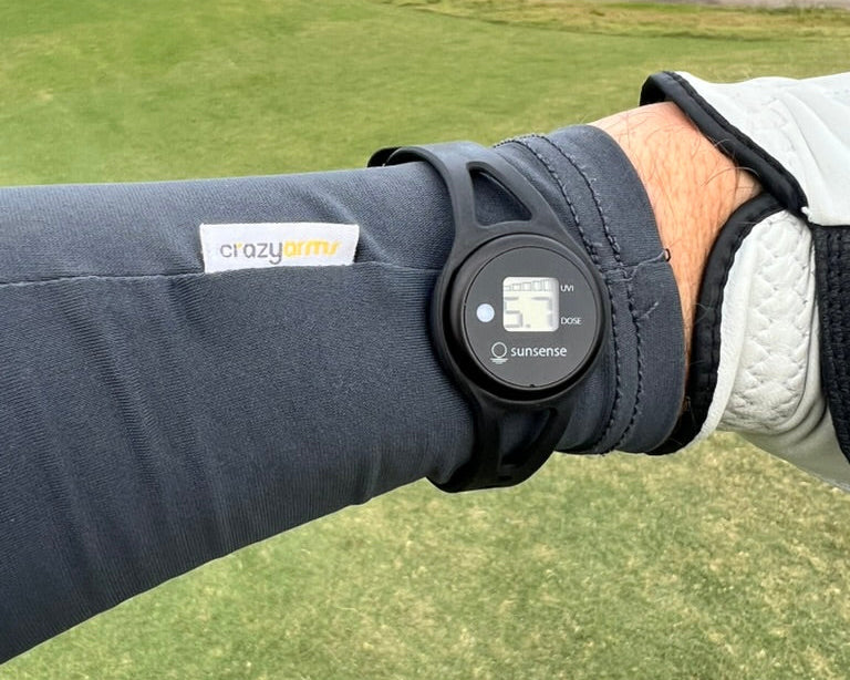 Golfer wearing a Crazy Arms sun sleeve with a UV meter on the wrist, on a coastal golf course
