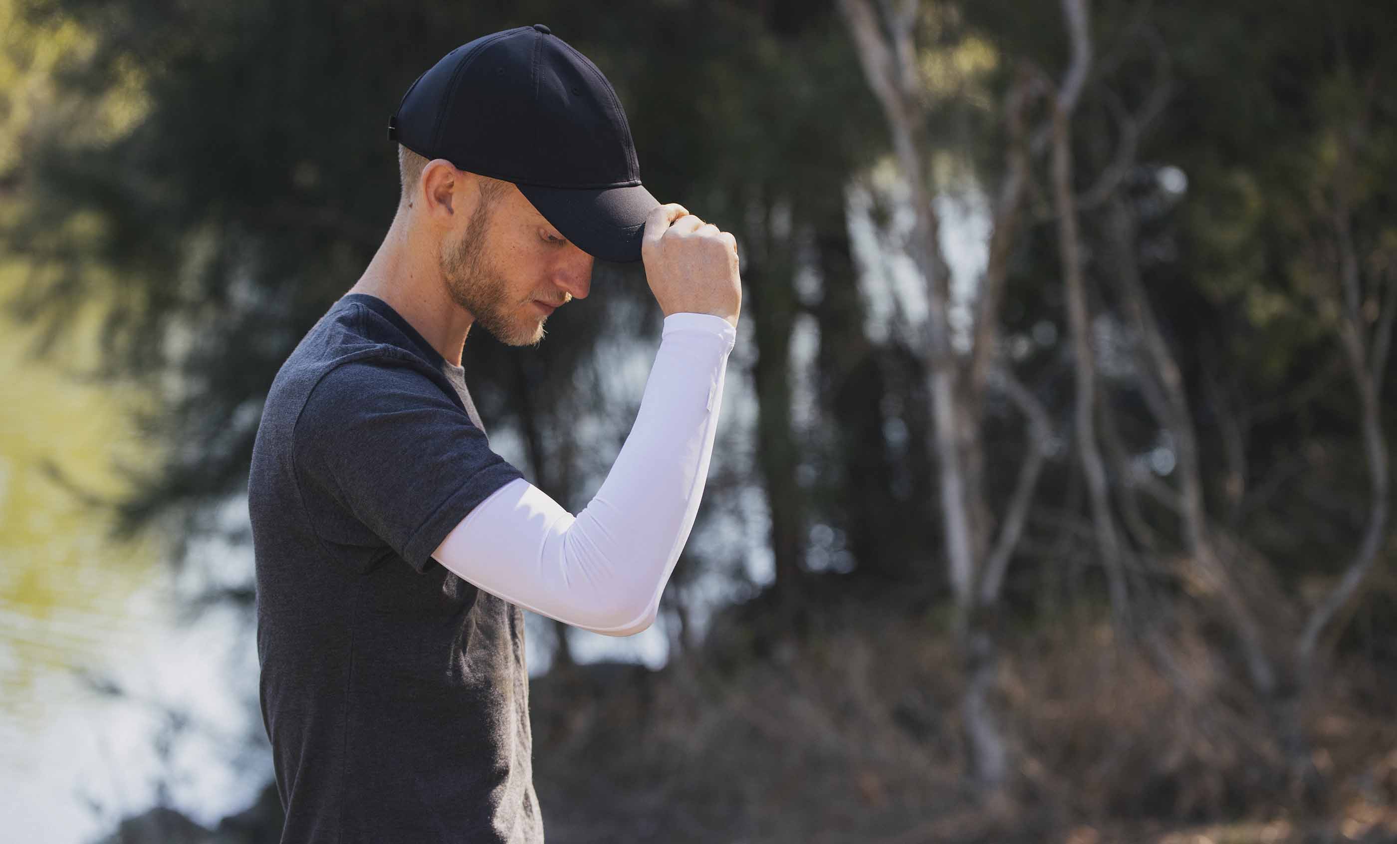 A stood in the outdoors man adjusting his cap wearing White Crazy Arms sun sleeves 