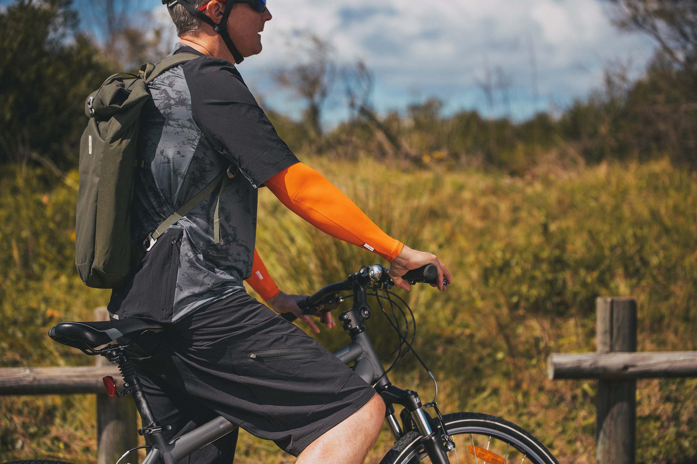 Man on push-bike in outdoors wearing sporty Orange Crazy Arms sun sleeves