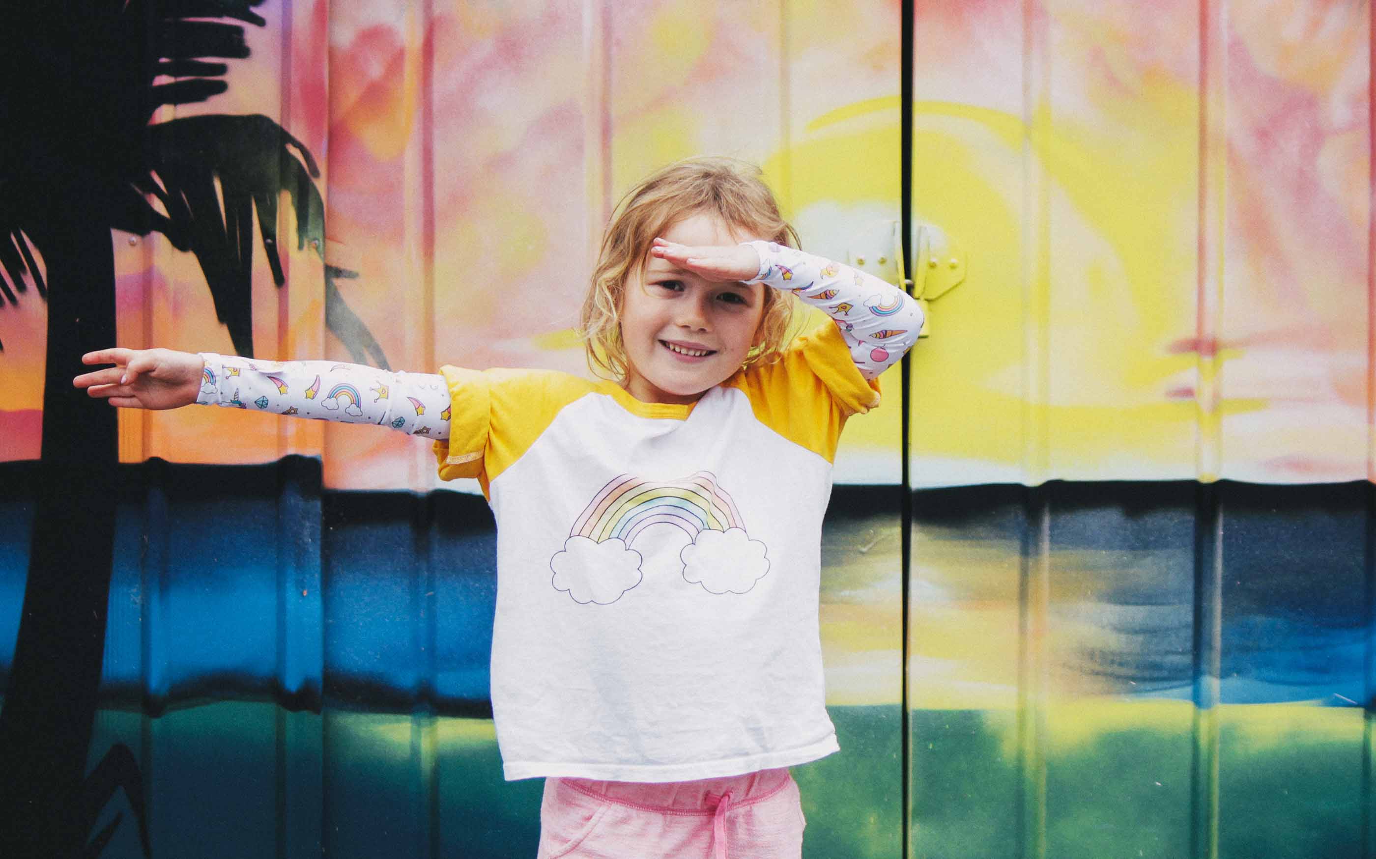 Girl standing in front of colourful background in a funny pose wearing Unicorn Crazy Arm sun sleeves