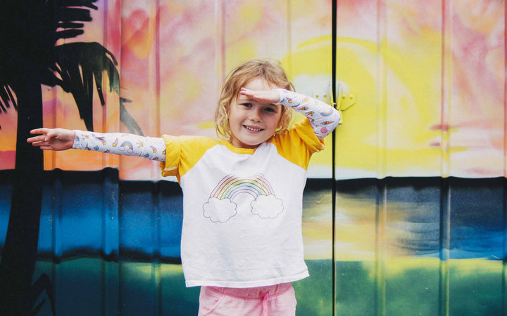 Girl standing in front of colourful background in a funny pose wearing Unicorn Crazy Arm sun sleeves