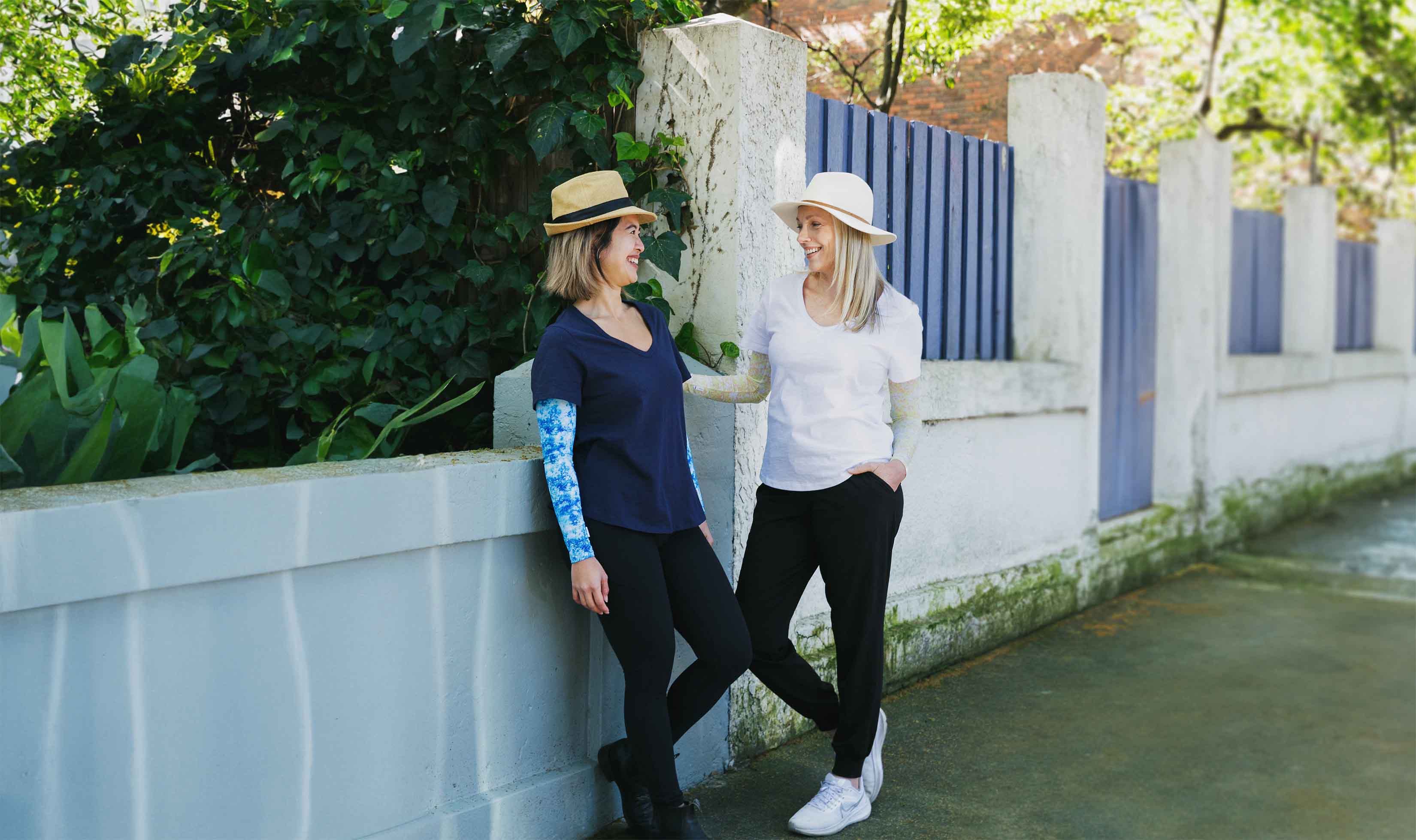 Two female friends engaging in friendly conversation on street wearing Crazy Arms sun protective sunsleeves