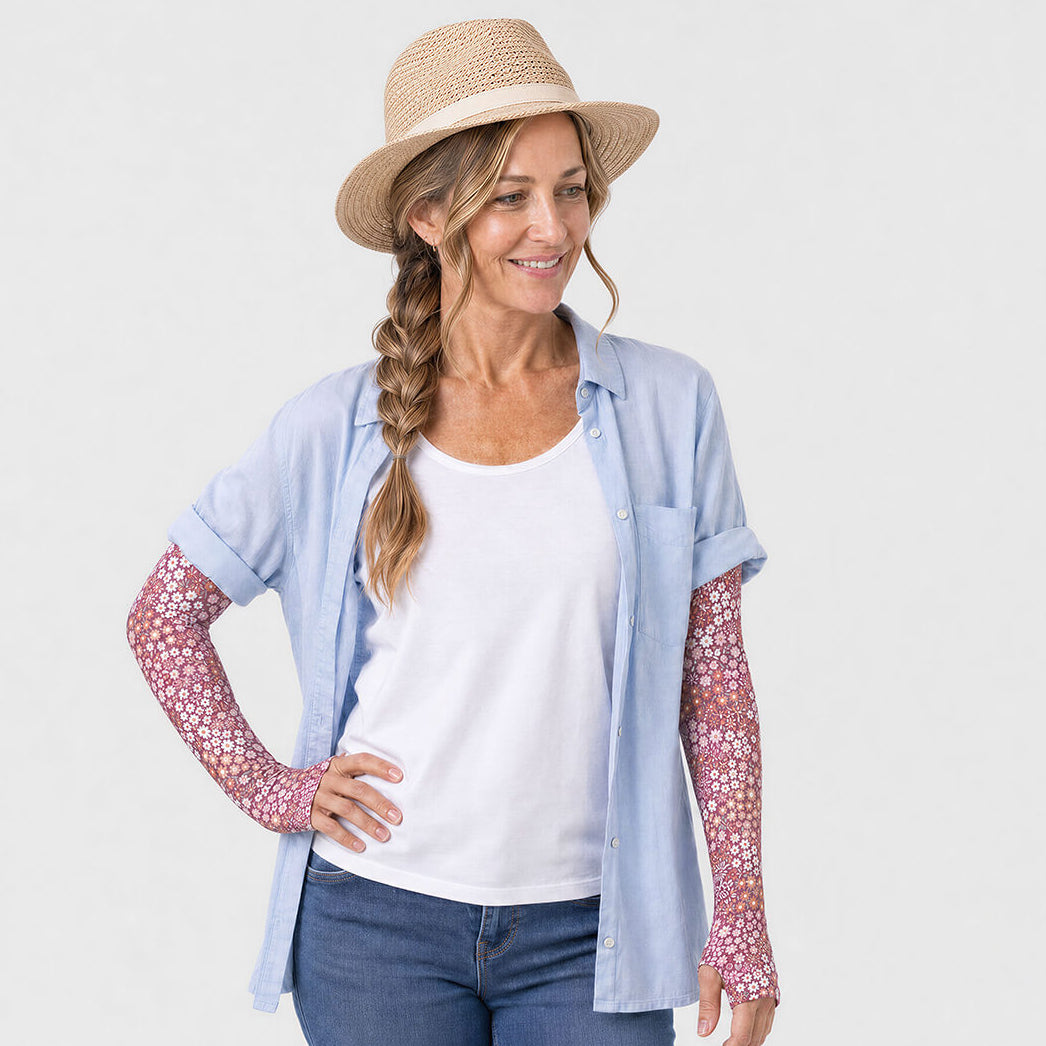 Woman wearing meadow floral sun sleeves, Meadow, with a blue shirt and white t-shirt
