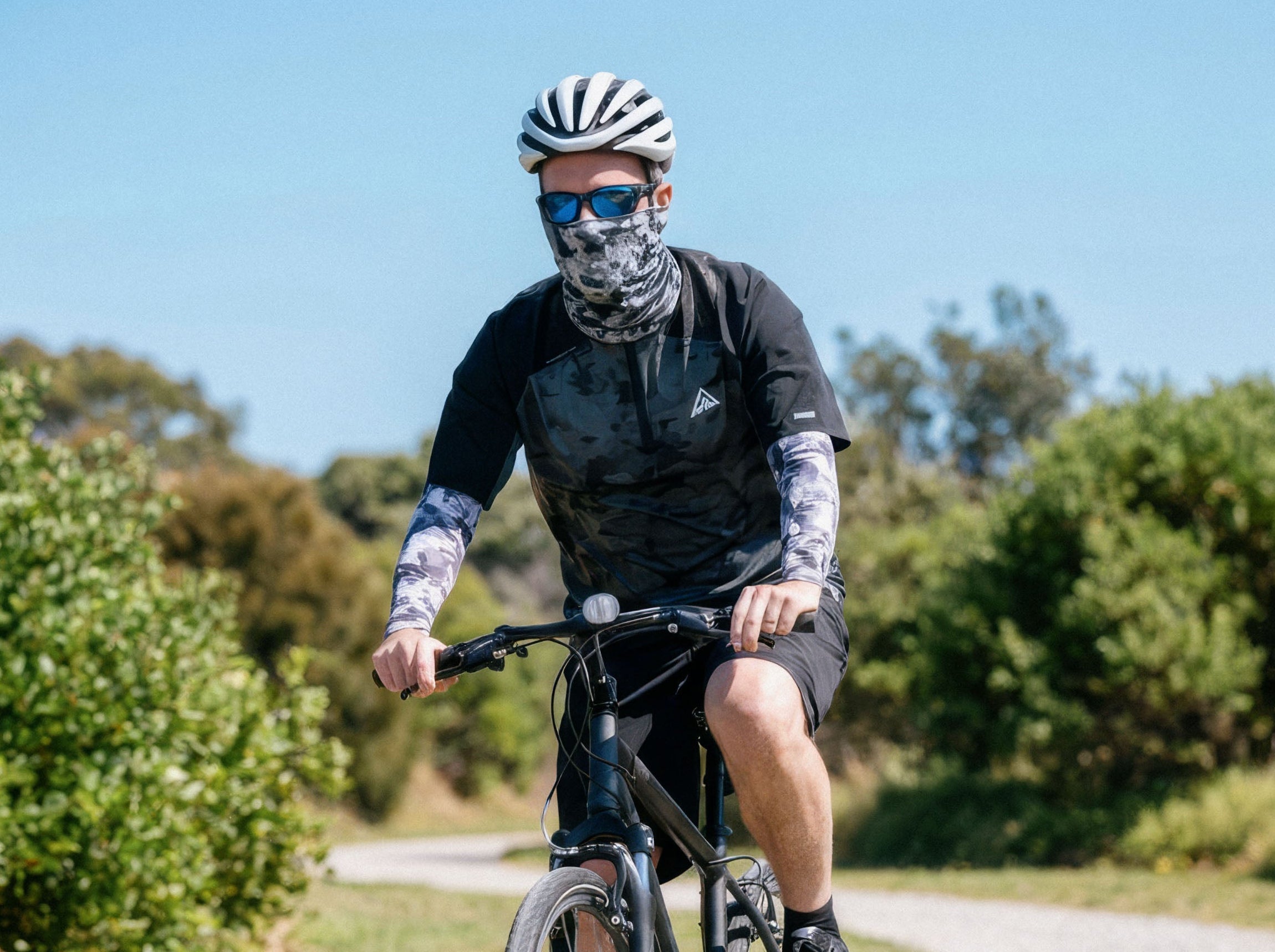 Man cycling in Crazy Arms grey camo sun sleeves and a matching Headskinz face and neck cover