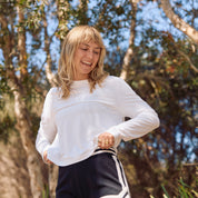 Woman in white UPF50+ long-sleeve top and black shorts outdoors with trees in the background
