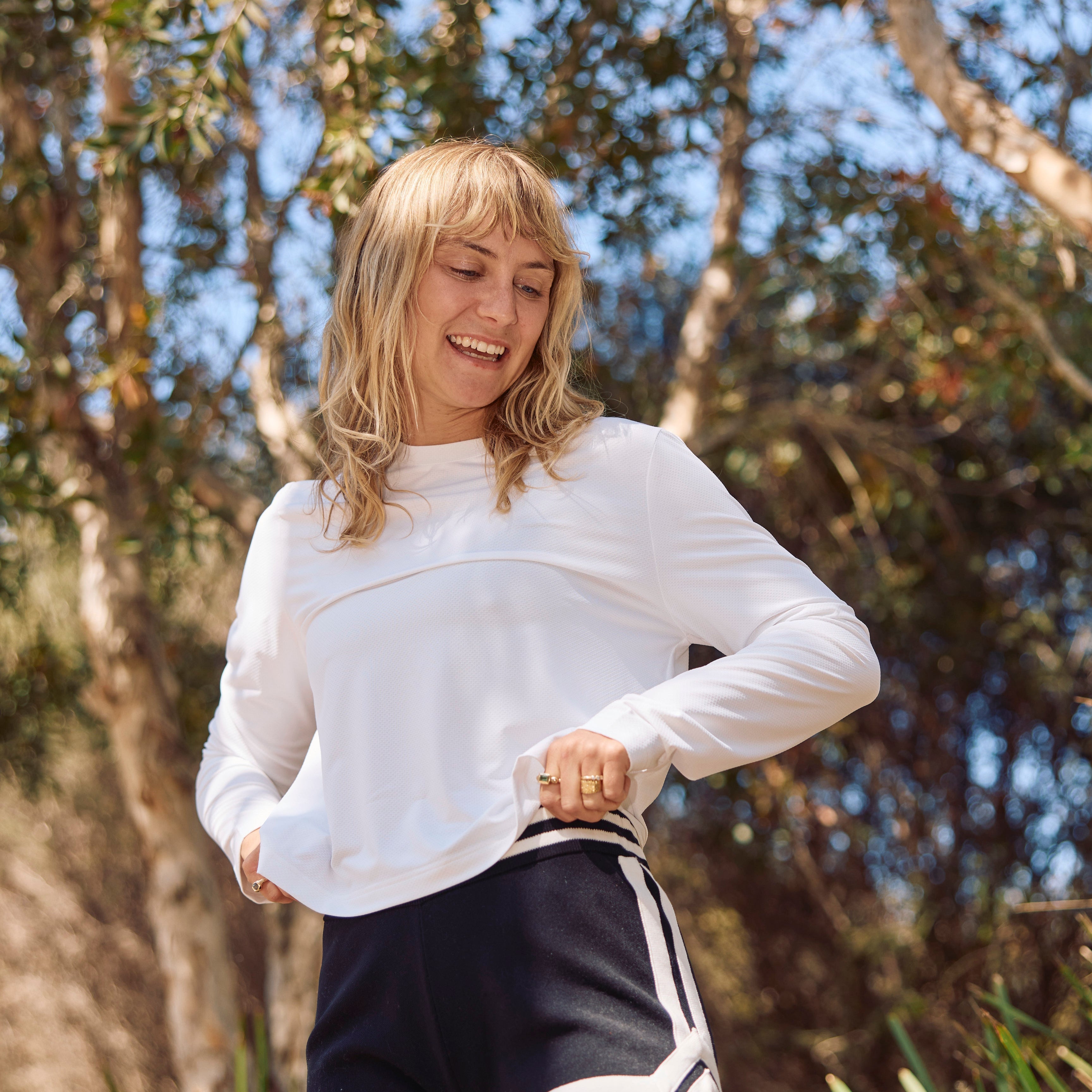 Woman in white UPF50+ long-sleeve top and black shorts outdoors with trees in the background