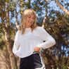 Woman in white UPF50+ long-sleeve top and black shorts outdoors with trees in the background