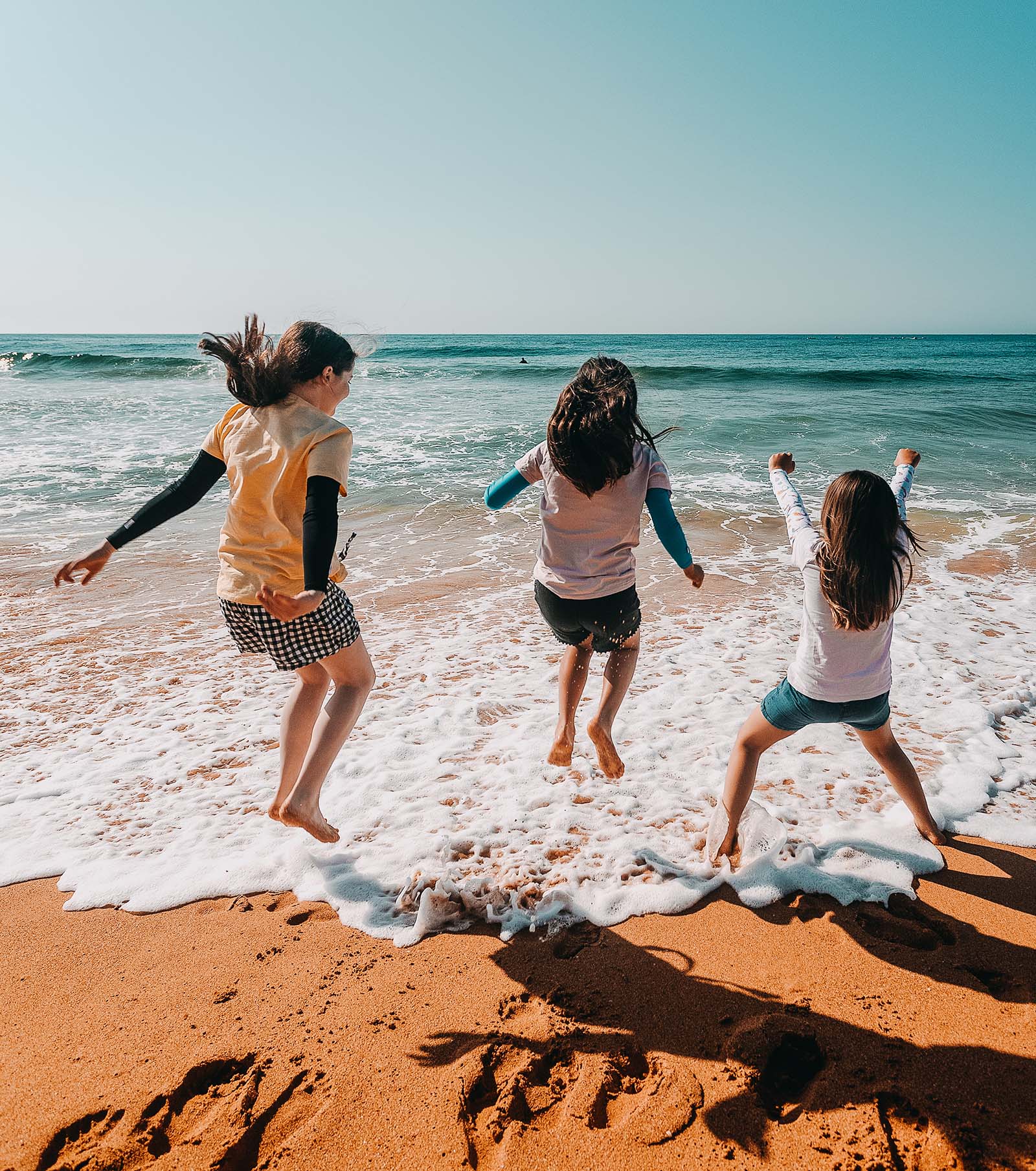 Kids wearing Crazy Arms sun sleeves on the beach and having fun jumping in the surf.